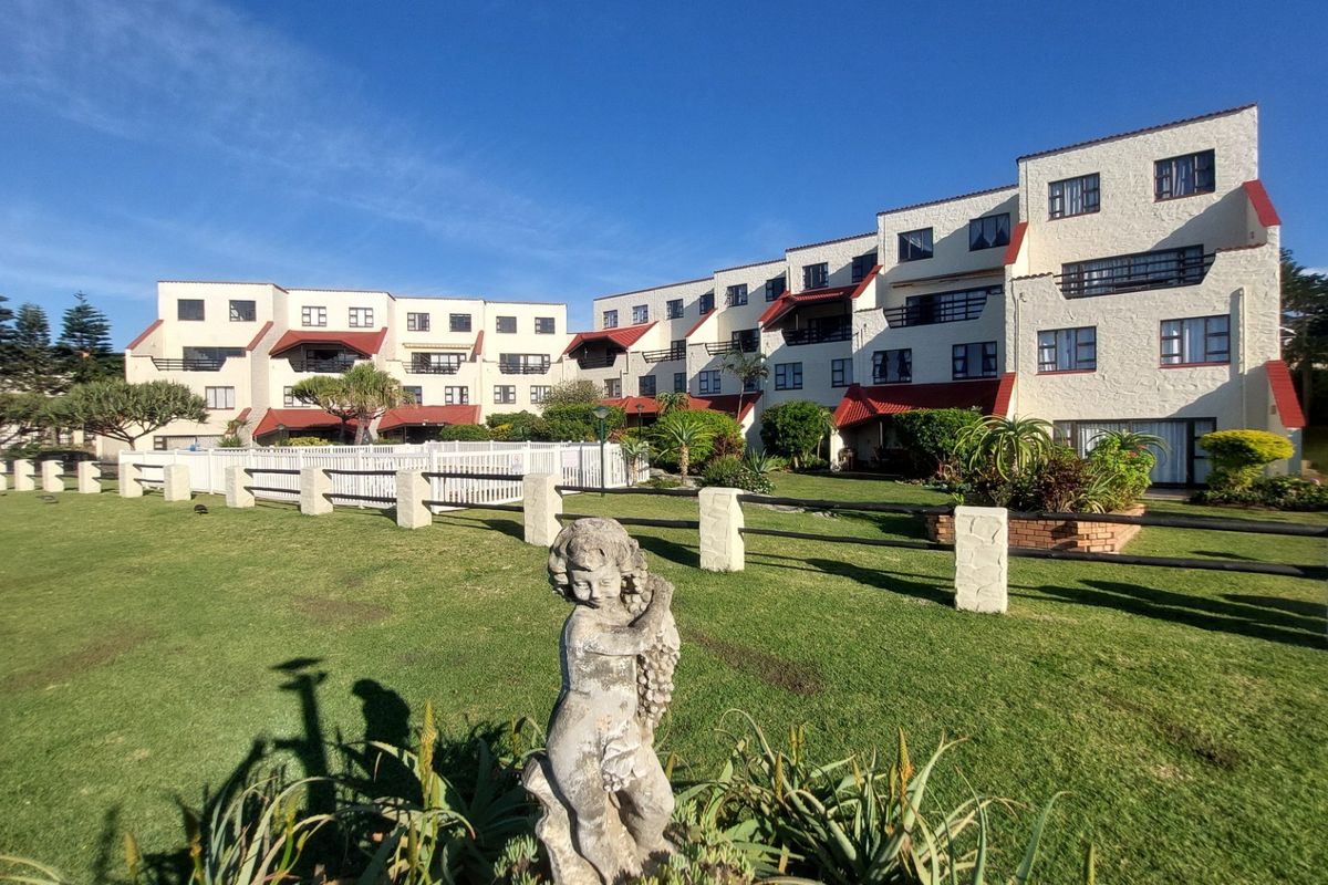 Exterior view of the apartment complex featuring a landscaped garden area, white perimeter fencing, and multi-story residential building blocks.