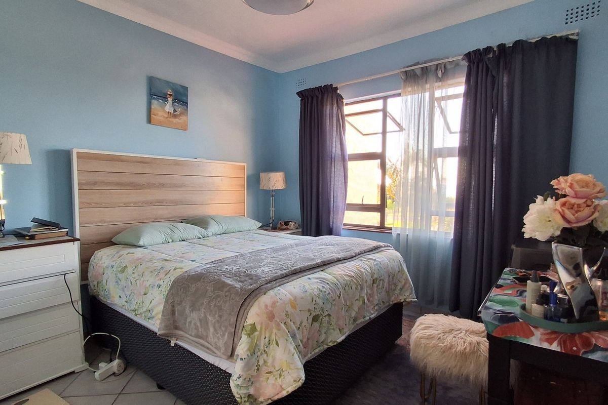 A bedroom featuring light blue walls, a large window with curtains, and a built-in headboard, providing a comfortable and functional sleeping space.