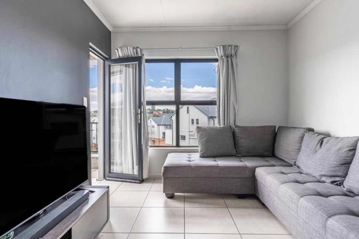 A bright living room featuring tiled flooring and direct access to a balcony through an aluminium door, offering natural light and exterior views.