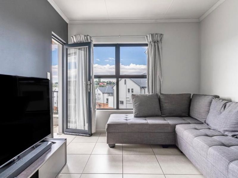 A bright living room featuring tiled flooring and direct access to a balcony through an aluminium door, offering natural light and exterior views.