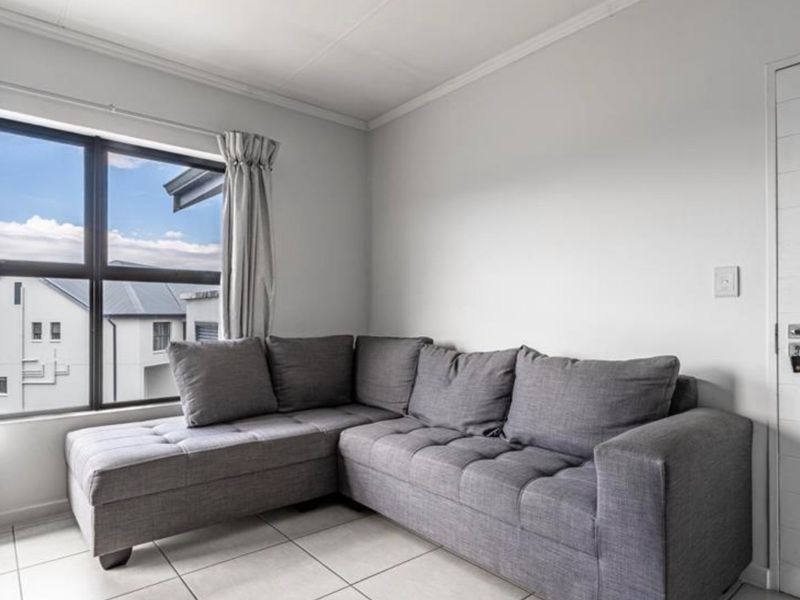 A bright living room featuring tiled flooring, neutral walls, and a large window providing natural light and exterior views.