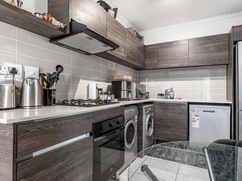 Modern kitchen featuring dark wood-grain cabinetry, stone countertops, tiled backsplash, and integrated appliances including a gas hob and oven.