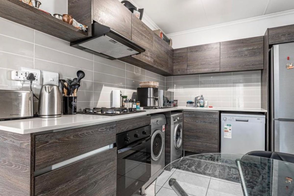 Modern kitchen featuring dark wood-grain cabinetry, stone countertops, tiled backsplash, and integrated appliances including a gas hob and oven.
