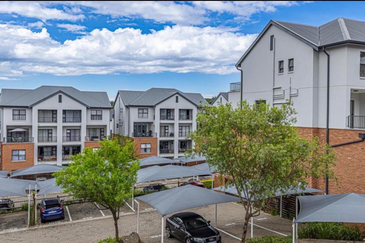 Exterior view of a modern apartment complex featuring brick and plaster facades, pitched roofs, and a paved parking area with shade cloth carports.