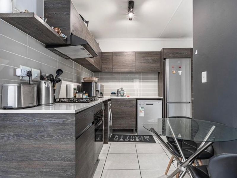 Modern kitchen featuring dark wood-grain cabinetry, stone countertops, tiled backsplash, gas hob, and integrated extractor fan, offering a sleek and functional cooking space.