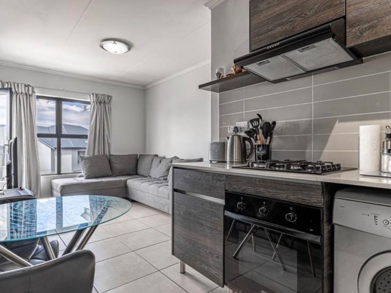 Modern open-plan living area featuring a compact kitchen with built-in cabinetry, gas hob, oven, and tiled flooring, seamlessly connected to the lounge space.