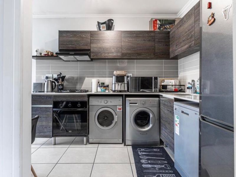 A functional kitchen featuring dark wood-grain cabinetry, tiled backsplash, built-in oven with gas hob, and integrated laundry appliance connections.