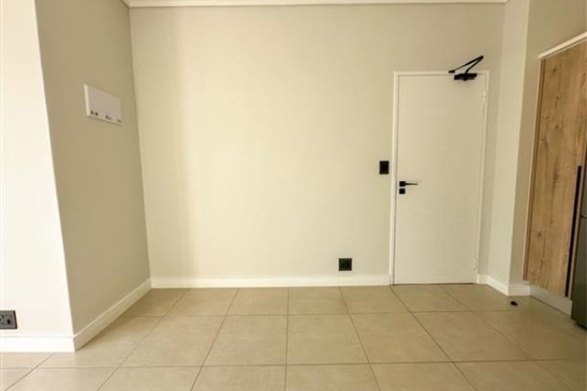 A clean, neutral-toned interior space featuring large format floor tiles, a modern internal door with a hydraulic closer, and built-in cabinetry.
