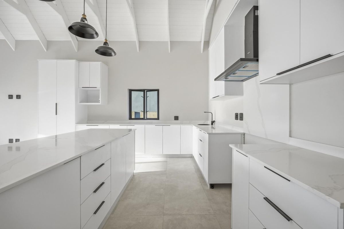Modern kitchen featuring white cabinetry, stone countertops, a central island, and vaulted ceilings with exposed beams.