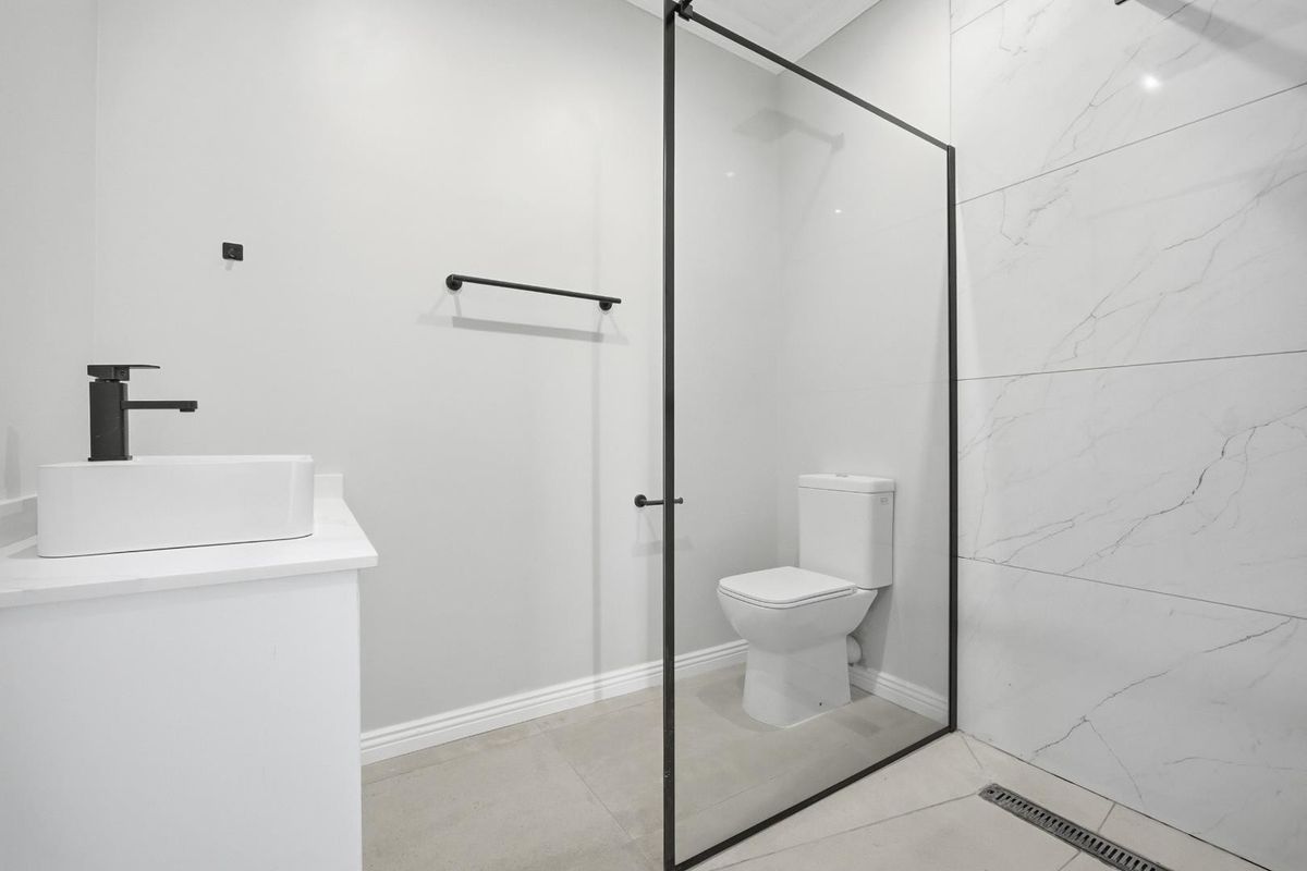 Modern bathroom featuring a walk-in shower with a black-framed glass screen, marble-look wall tiles, a contemporary vanity basin, and a toilet.