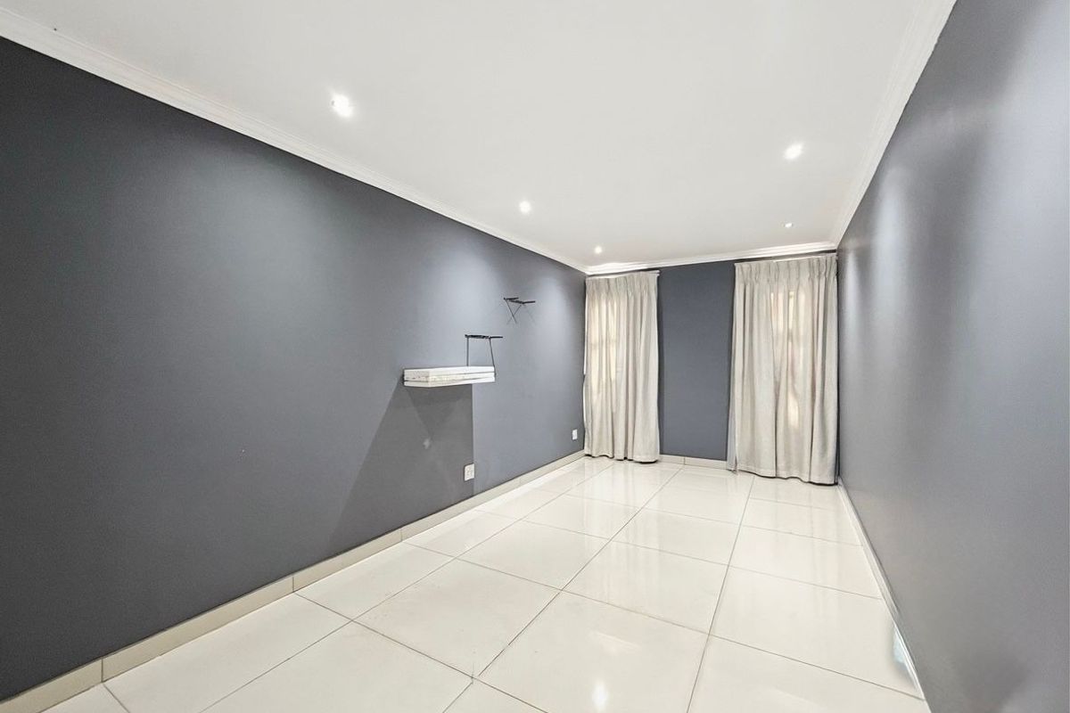 A bright, empty living room featuring modern grey walls, polished white floor tiles, recessed ceiling lighting, and floor-to-ceiling curtains.