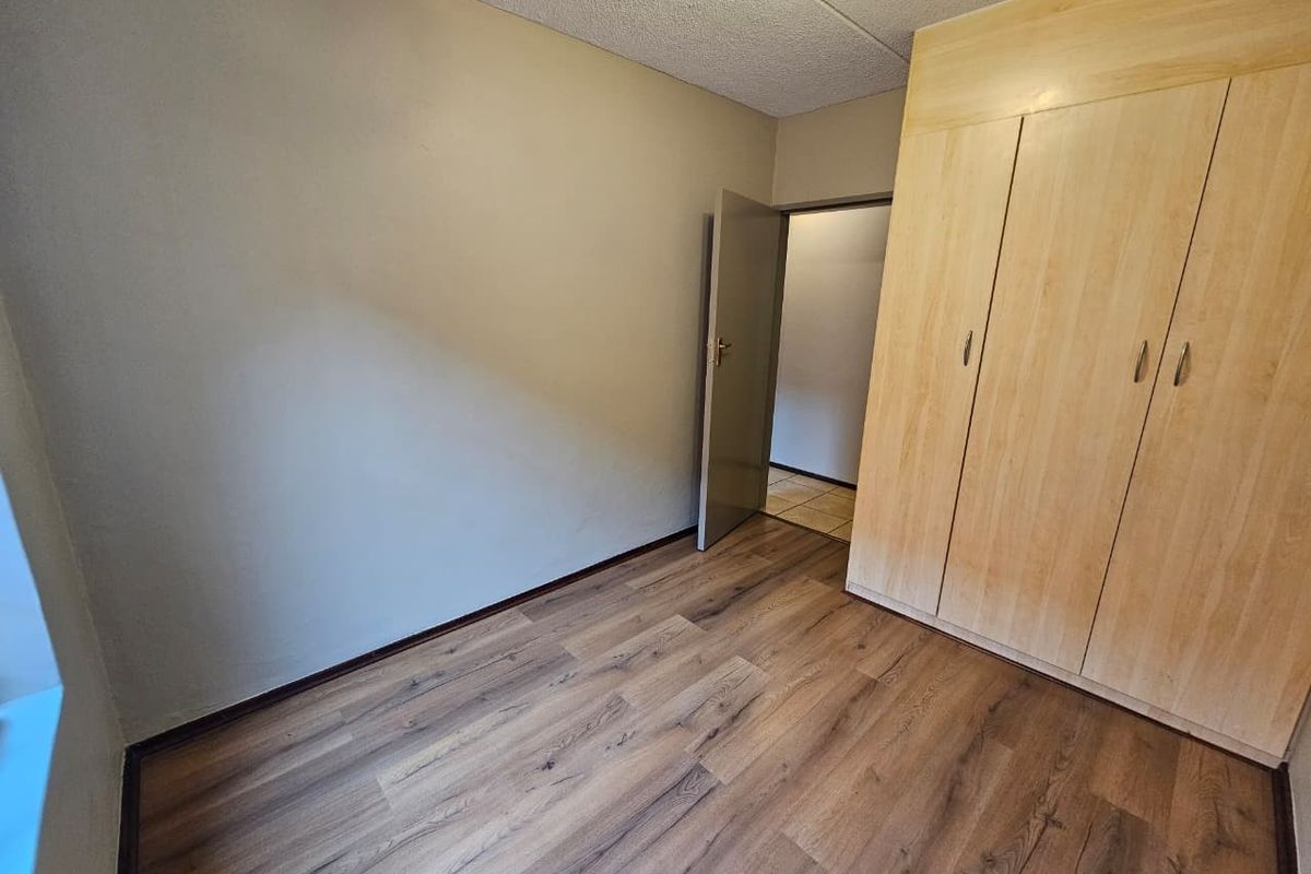 A vacant bedroom featuring light wood-finish built-in cupboards, modern laminate flooring, and neutral wall tones, offering a clean and versatile living space.