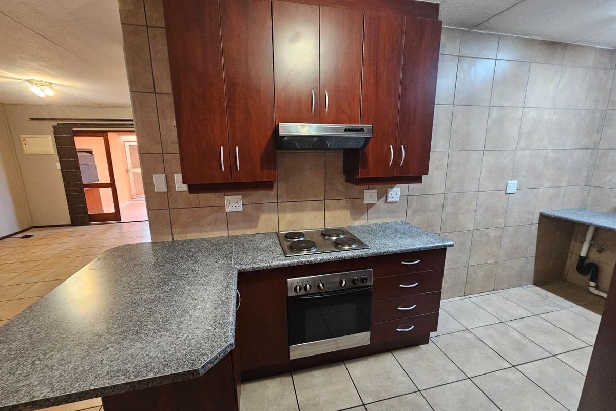 A functional kitchen featuring dark wood cabinetry, granite countertops, a built-in oven and hob, and tiled finishes throughout.