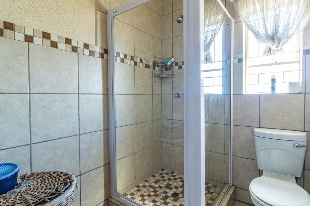 A functional bathroom featuring a glass-enclosed shower, ceramic wall tiling with decorative accents, and a standard white toilet.
