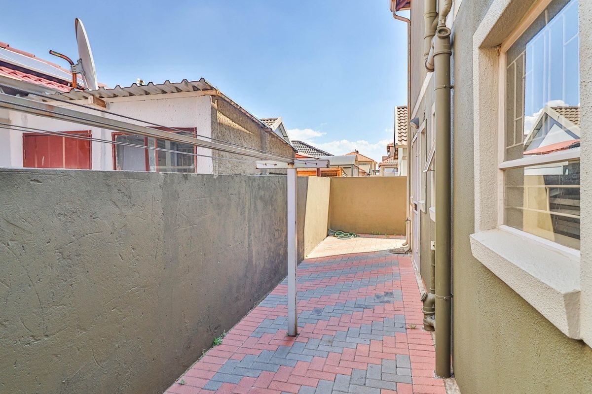 A side exterior walkway featuring paved flooring, a boundary wall, and a fixed washing line, providing functional outdoor utility space.