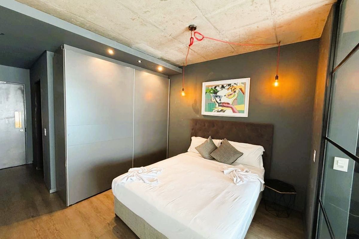 Modern bedroom featuring an exposed concrete ceiling, built-in floor-to-ceiling wardrobe, and industrial-style lighting.