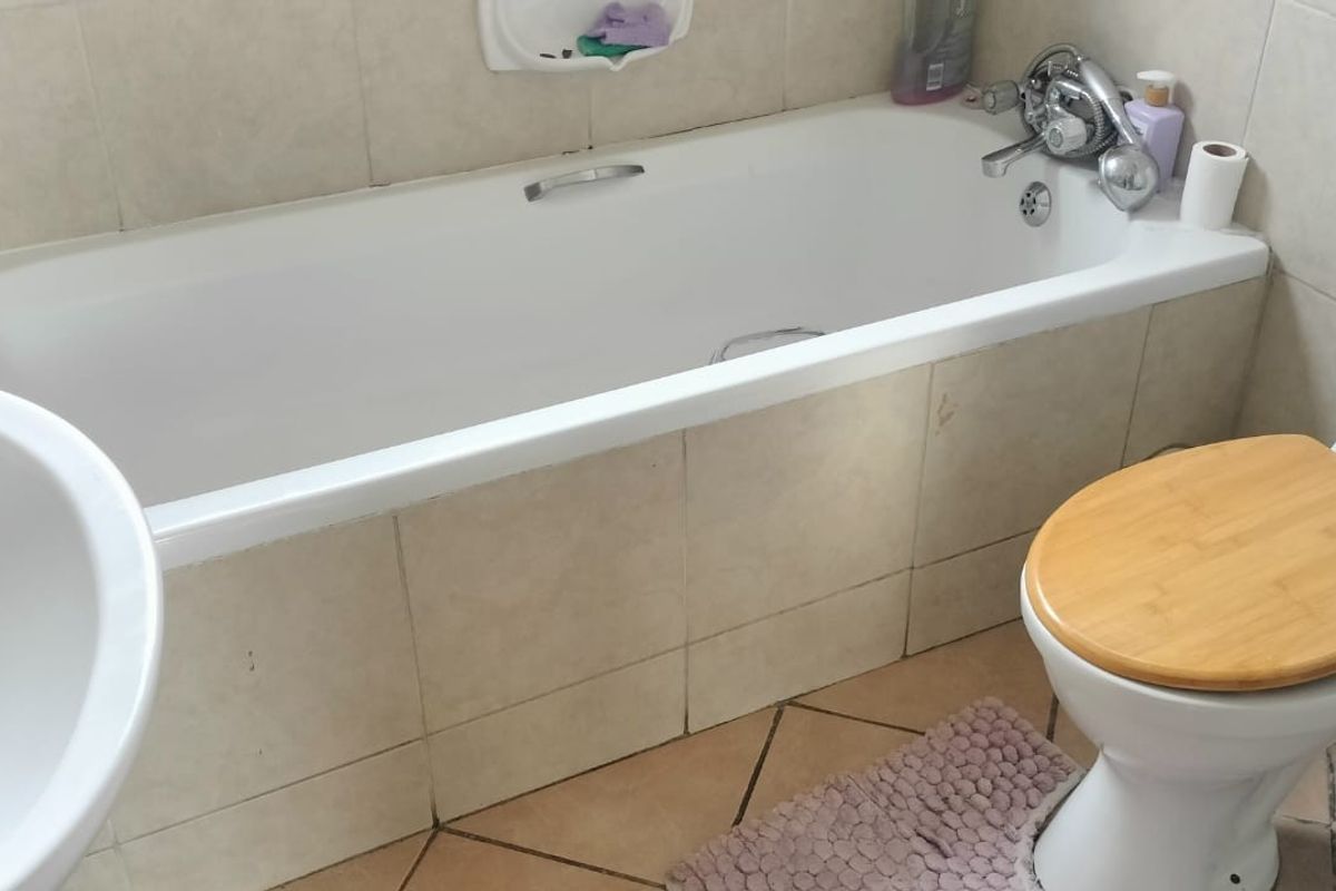 A functional bathroom featuring a standard bathtub, pedestal basin, and toilet with tiled walls and flooring.