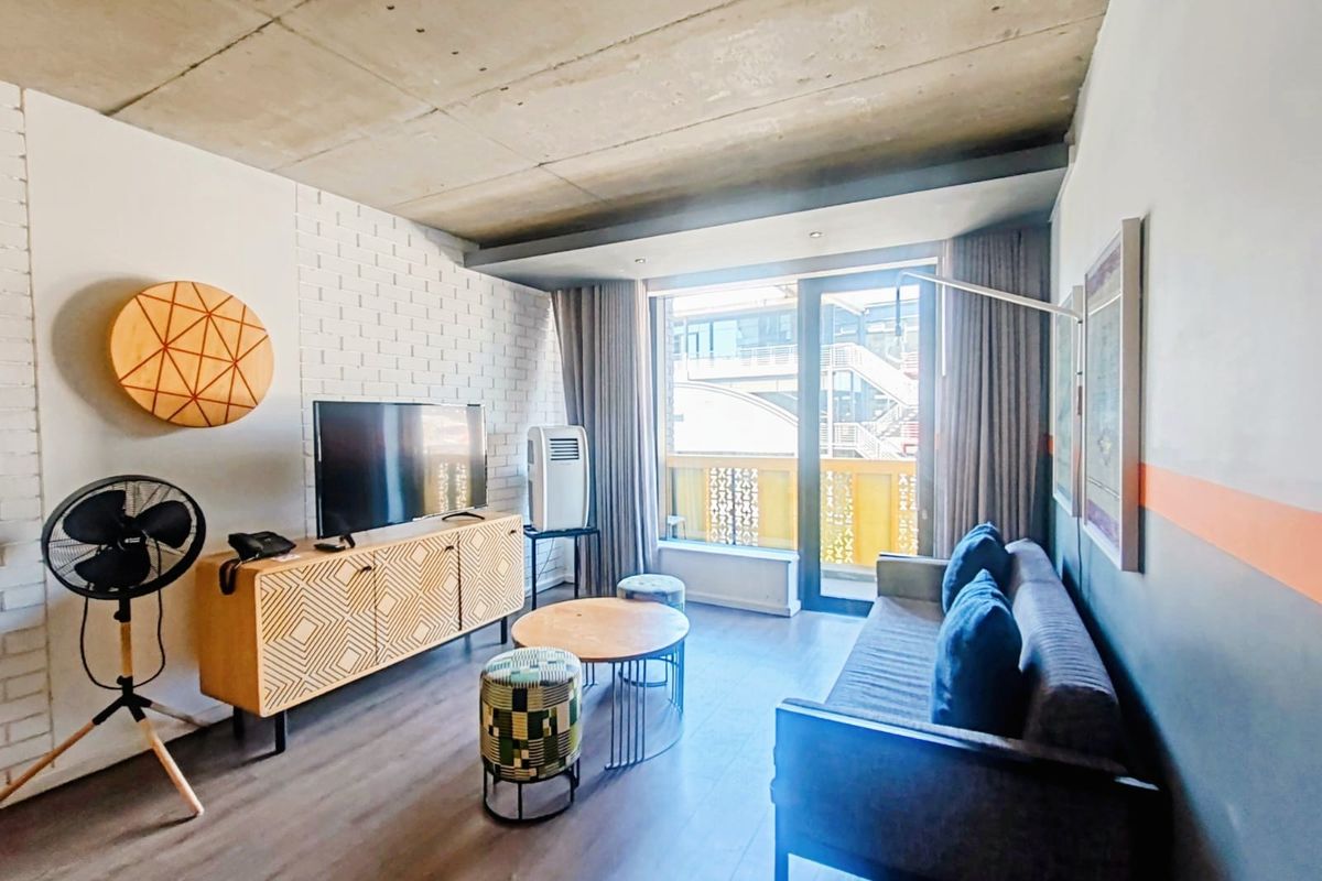Modern living room featuring an exposed concrete ceiling, brick accent wall, and large sliding glass doors leading to a balcony.