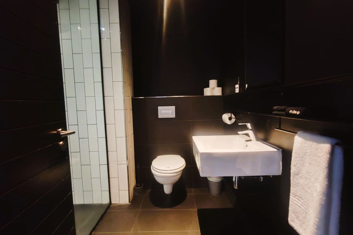 Modern bathroom featuring a wall-mounted basin, concealed cistern toilet, and a walk-in shower with white subway tiling against dark wall finishes.