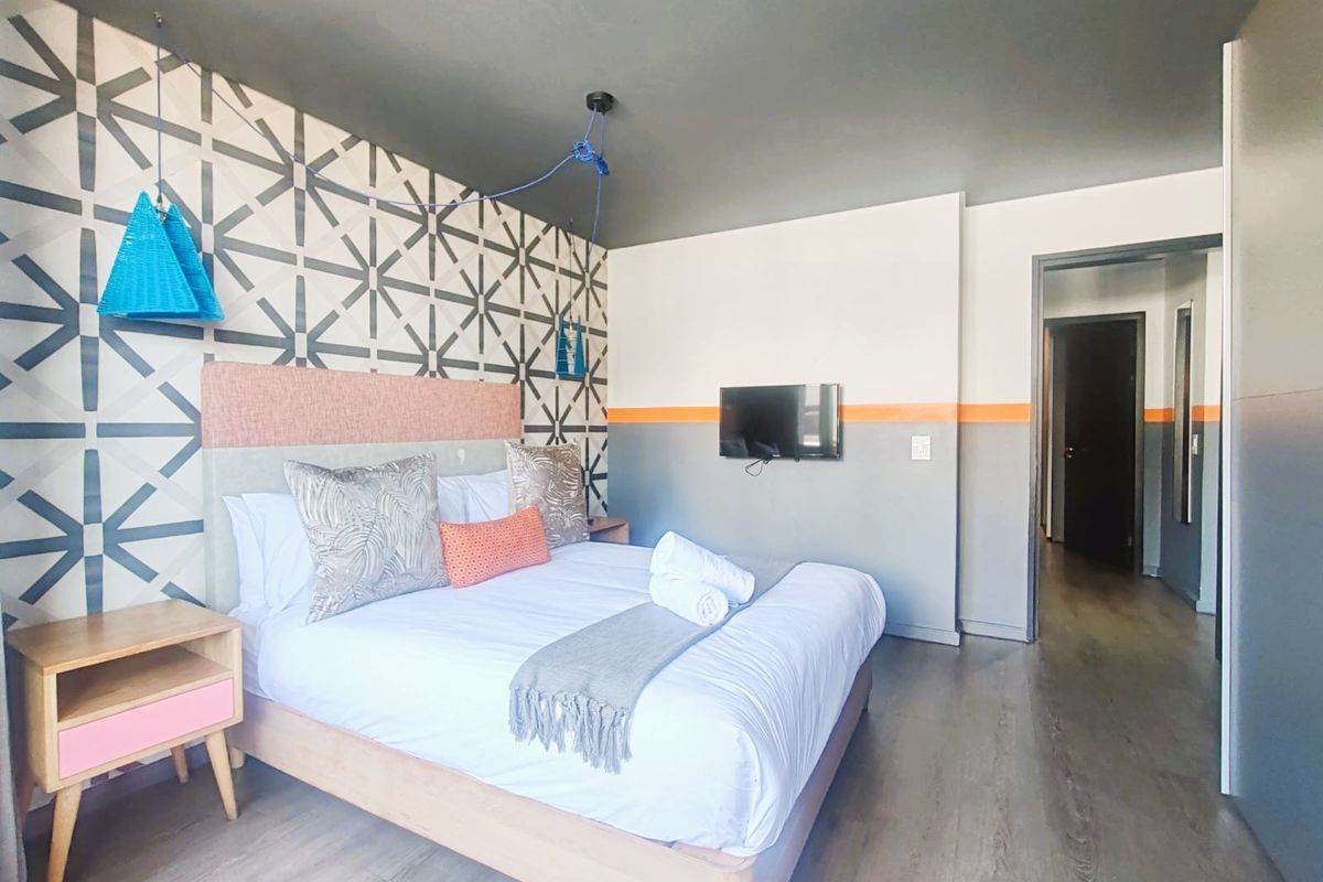 A modern bedroom featuring laminate flooring, a decorative patterned accent wall, and a wall-mounted television.