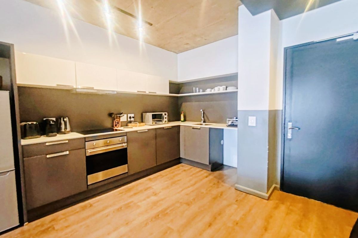 Modern kitchen featuring sleek grey cabinetry, stainless steel appliances, laminate flooring, and an industrial-style exposed concrete ceiling.