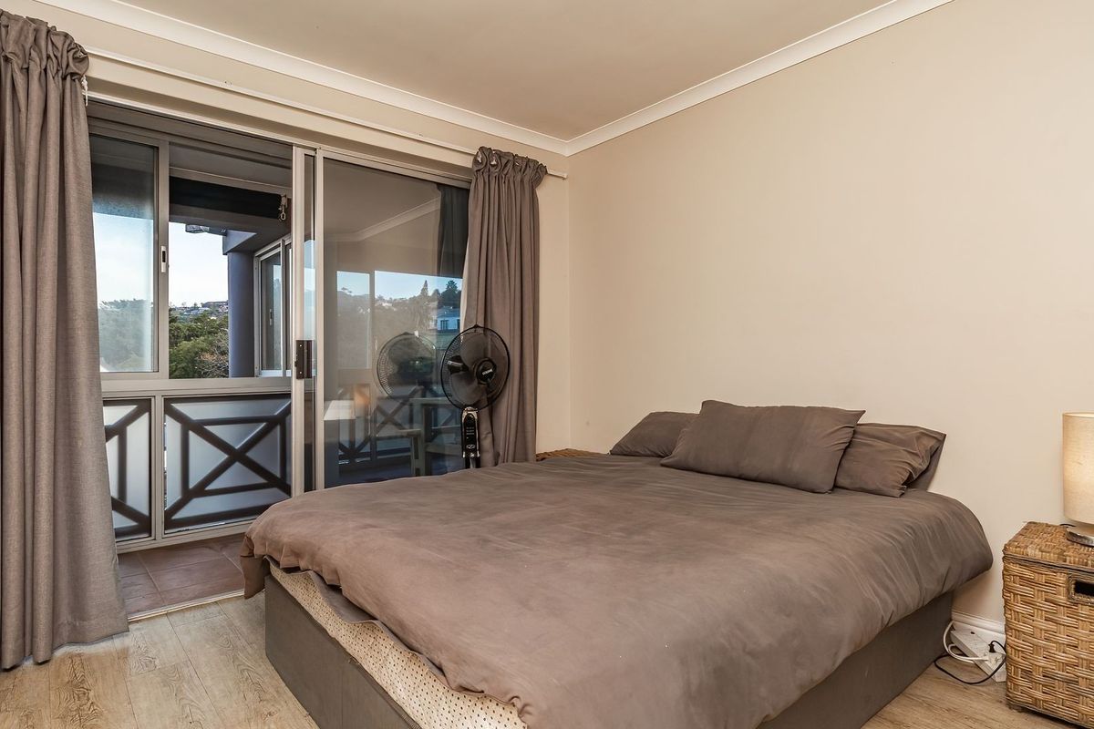 A bedroom featuring light wood-look flooring, neutral walls, and a sliding glass door providing access to a private balcony.
