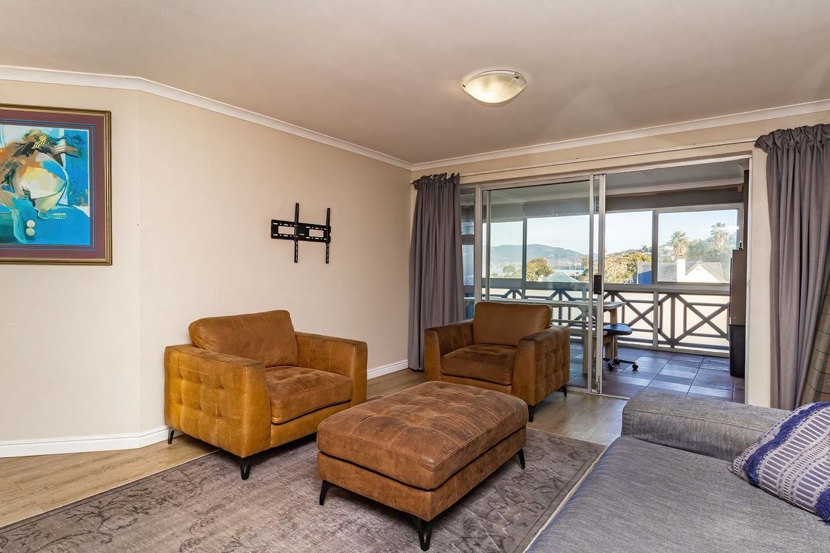 A comfortable living room featuring laminate flooring, coved ceilings, and large sliding glass doors that open onto a private balcony with scenic views.