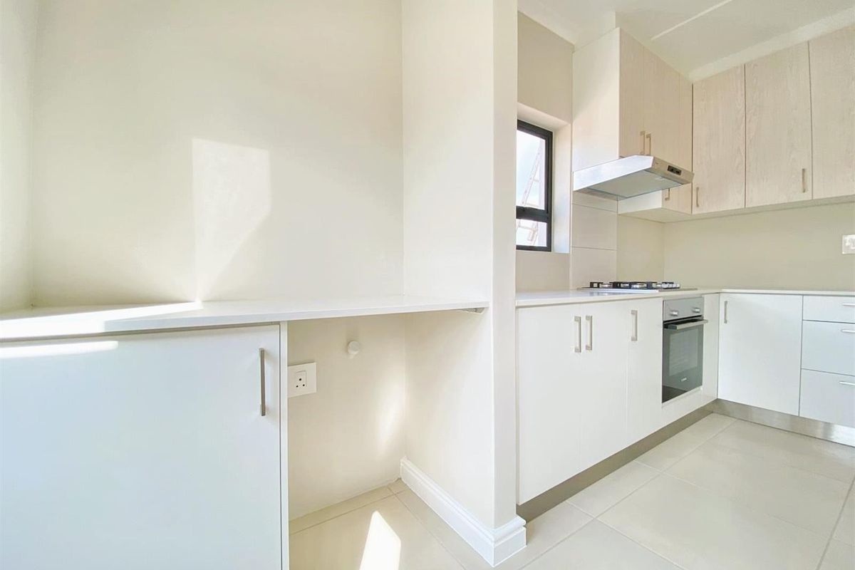 Modern kitchen featuring light-toned cabinetry, stone countertops, built-in oven, gas hob, and extractor fan with tiled flooring.