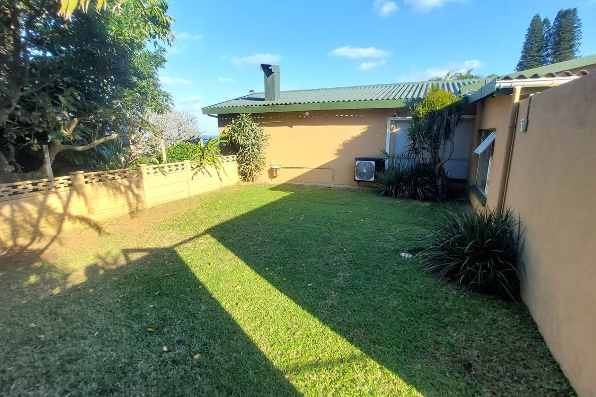 A private rear garden area featuring a lawn, perimeter boundary wall, and exterior building elevation with an installed air conditioning unit.