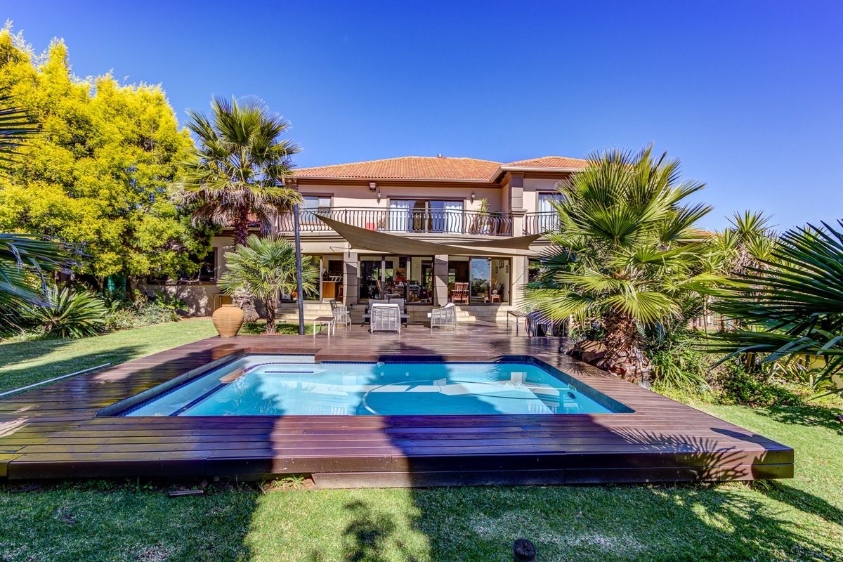 Rear view of the property featuring a swimming pool with timber decking, a landscaped garden, and an upper-level balcony.