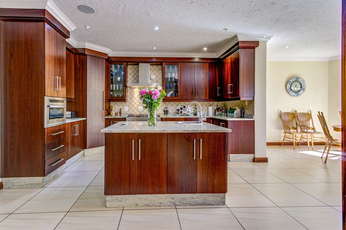 Spacious kitchen featuring dark wood cabinetry, granite countertops, a central island with a sink, and integrated appliances, finished with neutral floor tiles.