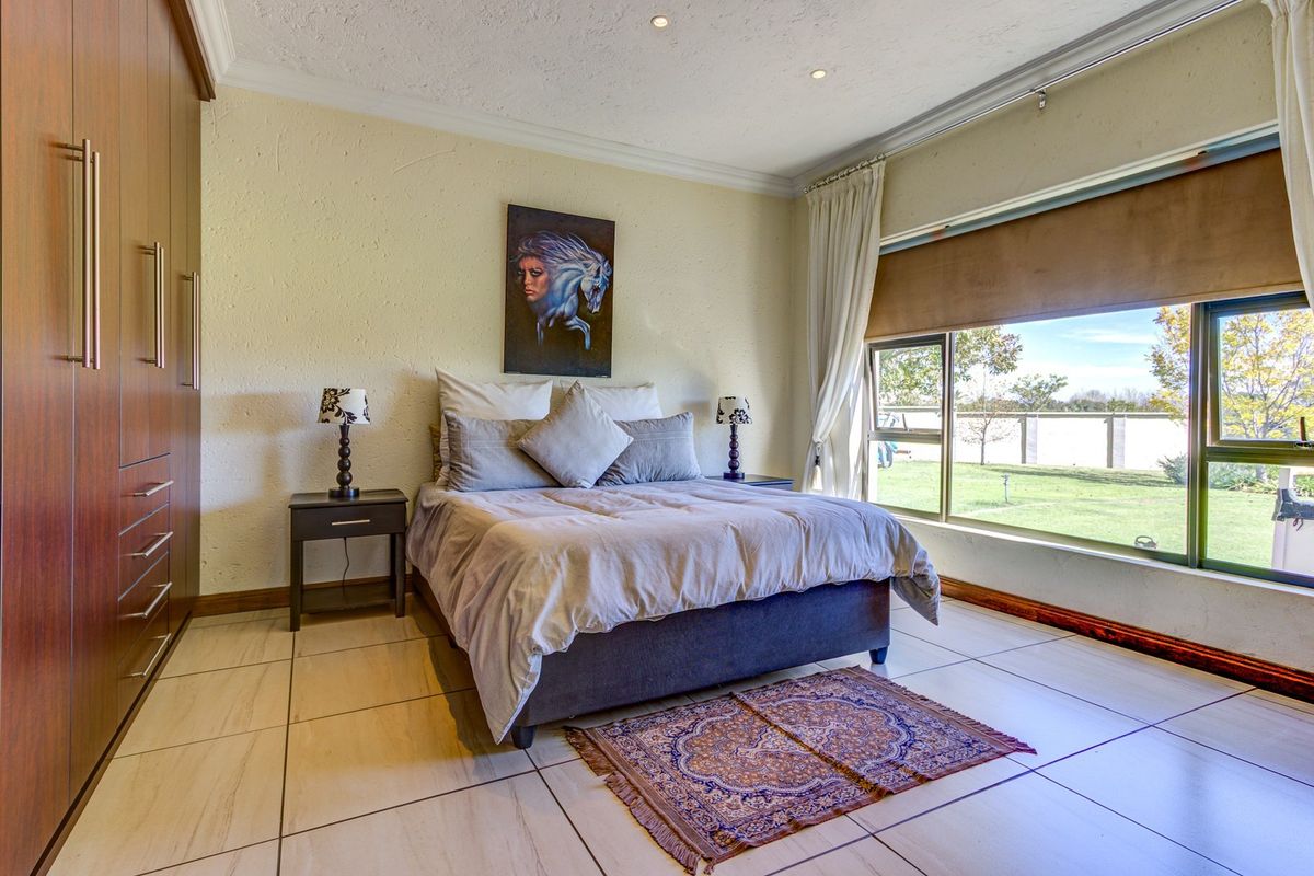 A well-lit bedroom featuring tiled flooring, built-in cupboards, and a large window offering views of the garden.