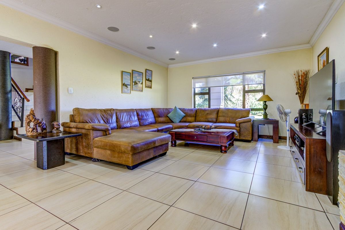 Spacious living room featuring neutral tiled flooring, recessed downlighting, integrated ceiling speakers, and a view towards the staircase.
