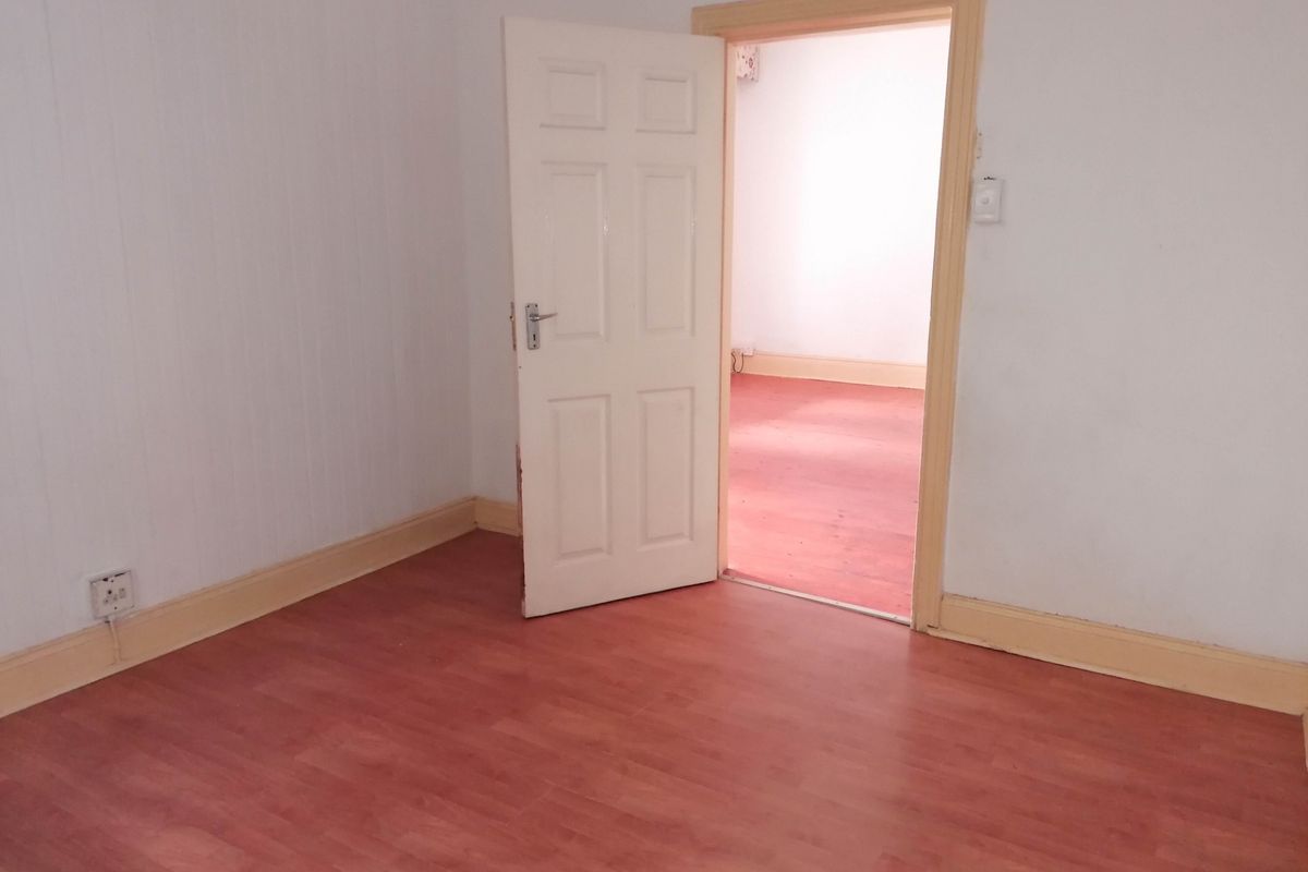 An empty bedroom featuring wood-look laminate flooring, white panelled walls, and a traditional interior door leading to an adjacent room.