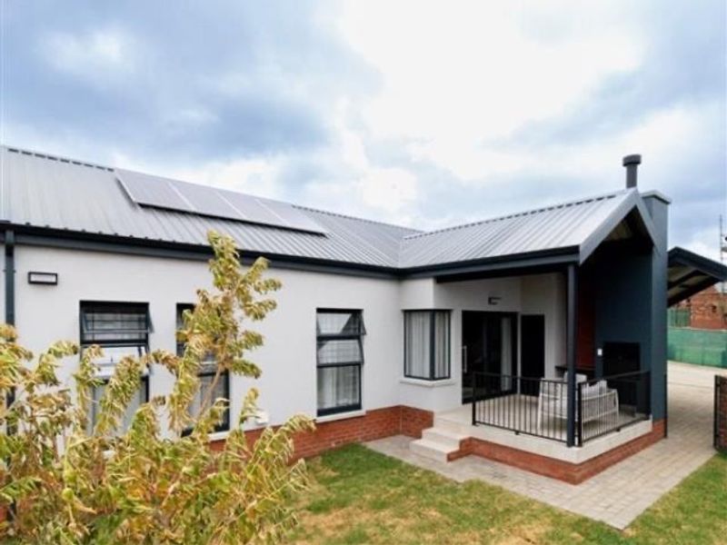 Rear view of the townhouse featuring a covered patio, metal roofing with integrated solar panels, and a paved outdoor area.