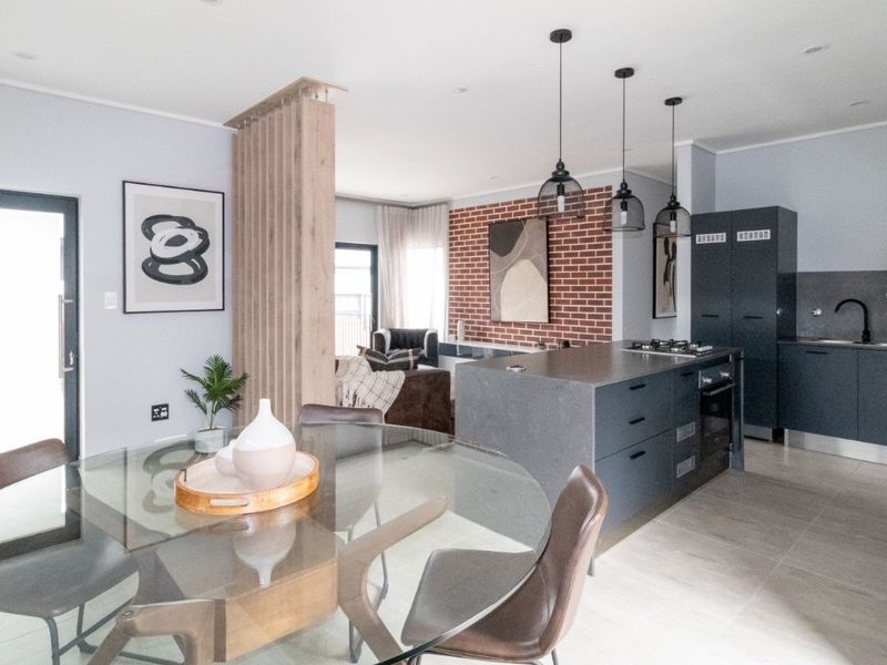Modern open-plan living area featuring a sleek kitchen island, exposed brick accent wall, timber slat divider, and contemporary pendant lighting throughout the space.