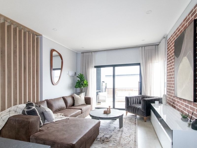 Modern living room featuring an exposed brick accent wall, timber slat detailing, recessed lighting, and large sliding doors leading to an outdoor patio area.