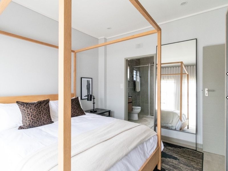 A modern, well-maintained bedroom featuring neutral tones, recessed lighting, and an adjoining en-suite bathroom with contemporary finishes.