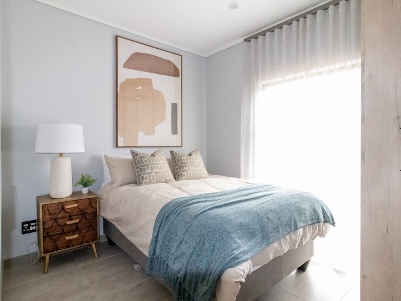 A well-maintained bedroom featuring neutral wall tones, tiled flooring, and natural light filtered through sheer curtains.