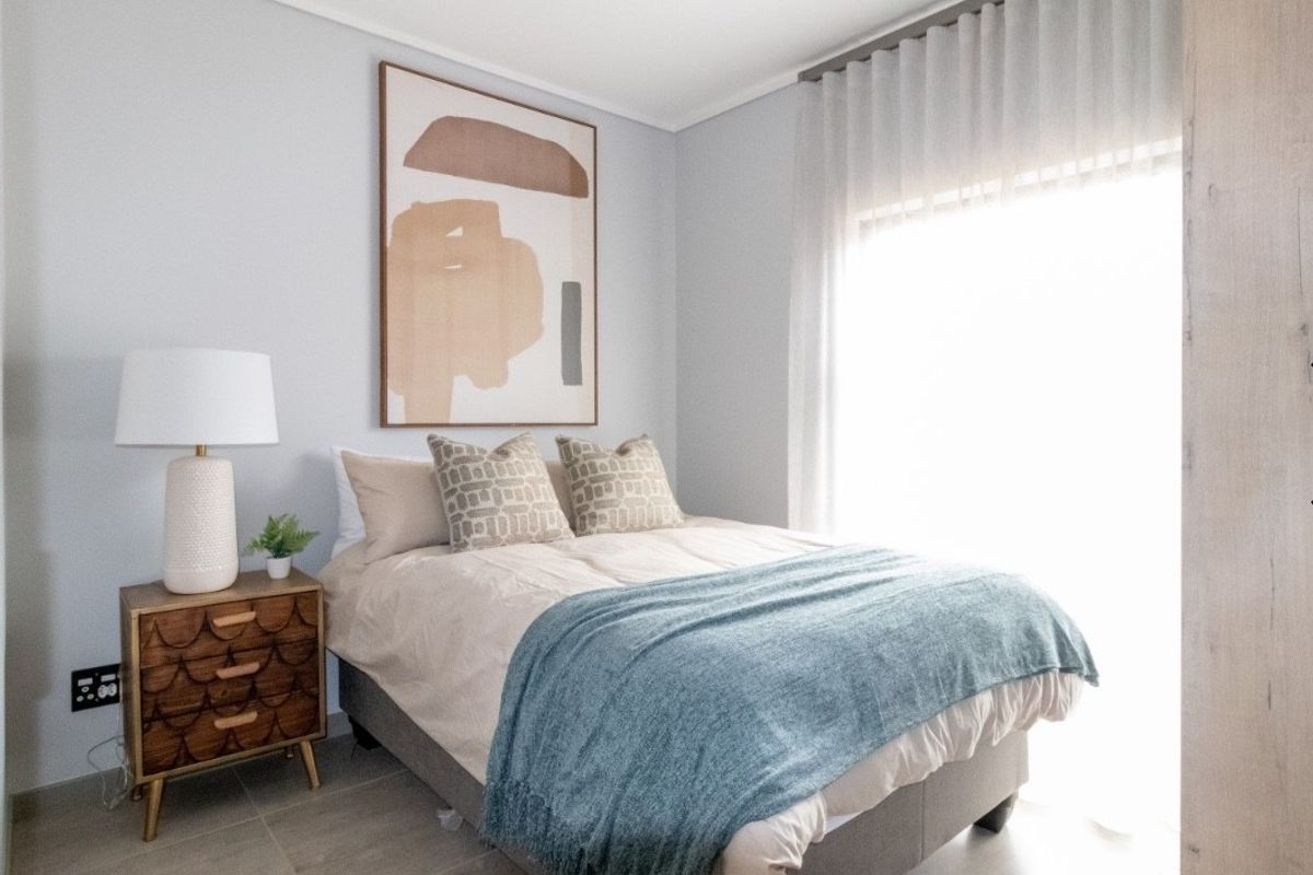 A well-maintained bedroom featuring neutral wall tones, tiled flooring, and natural light filtered through sheer curtains.