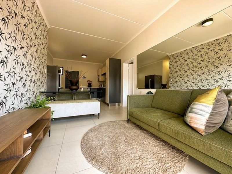 An open-plan living and kitchen area featuring tiled floors, a large wall mirror, and modern cabinetry, creating a bright and functional living space.