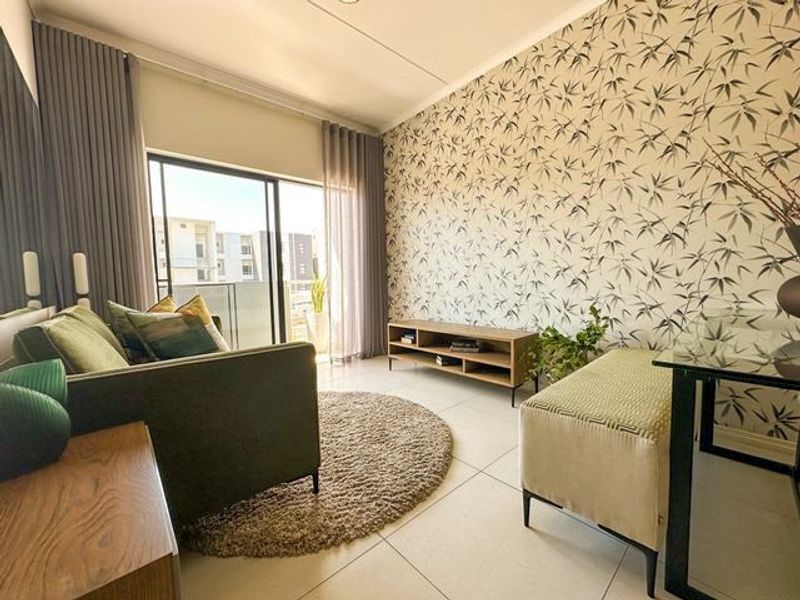 A bright living room featuring large sliding glass doors leading to a balcony, neutral tiled flooring, and a decorative feature wall.