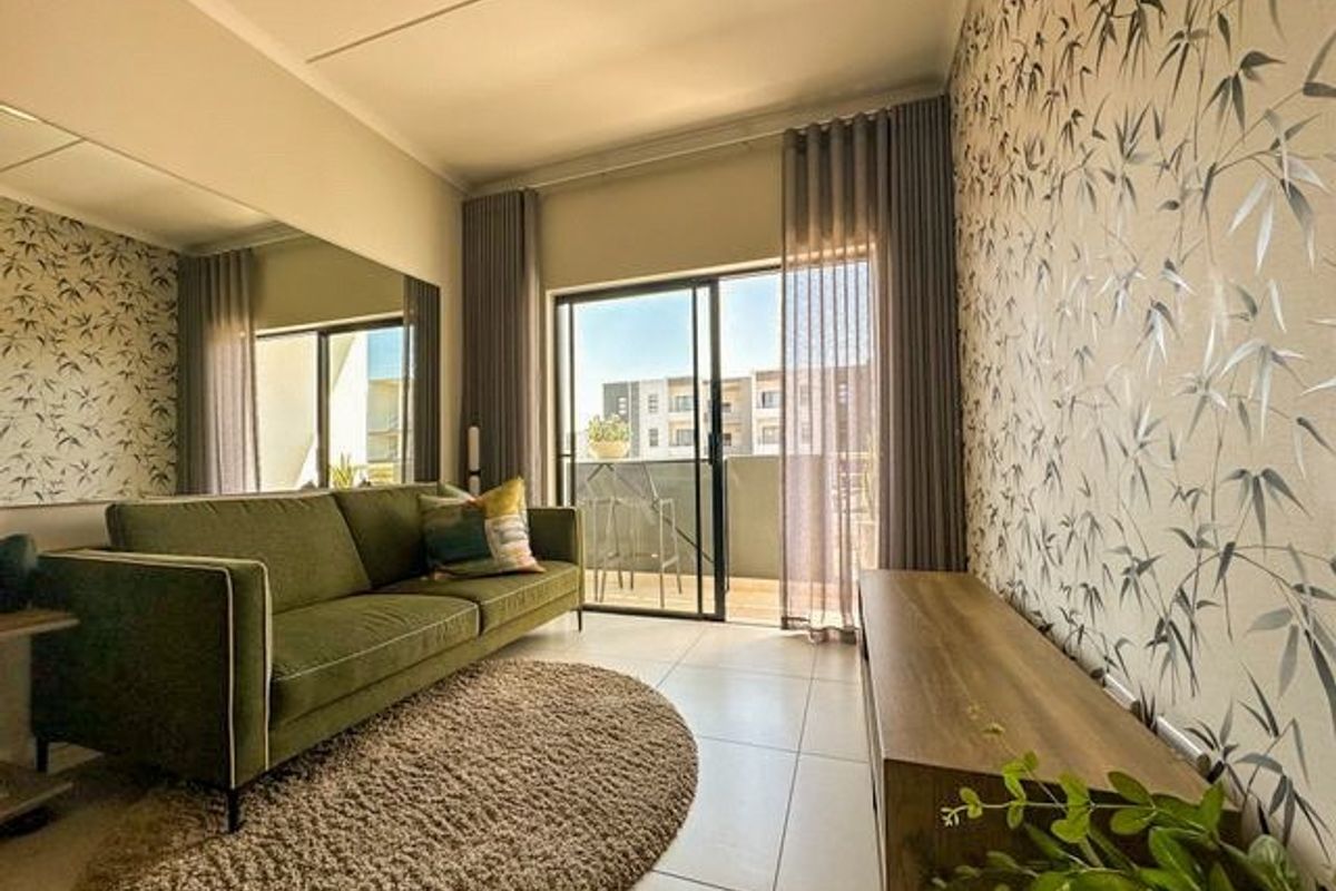 A well-lit living room featuring large sliding glass doors leading to a balcony, tiled flooring, and a decorative feature wall.