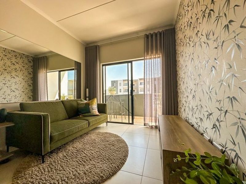 A well-lit living room featuring large sliding glass doors leading to a balcony, tiled flooring, and a decorative feature wall.