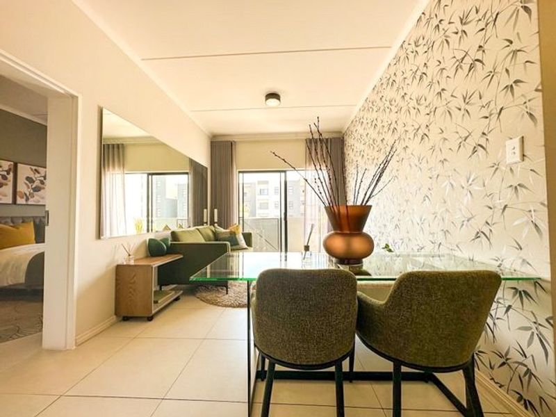 Open plan living and dining area featuring tiled floors, a large wall mirror, and a feature wallpaper wall with access to a balcony.