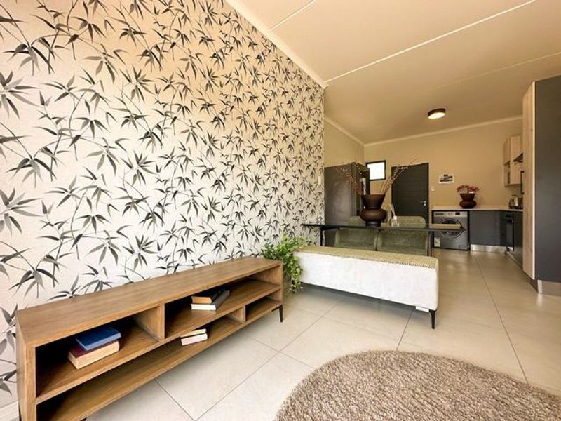 Open-plan living and kitchen area featuring tiled flooring, patterned feature wall, and modern built-in kitchen cabinetry with integrated appliances.