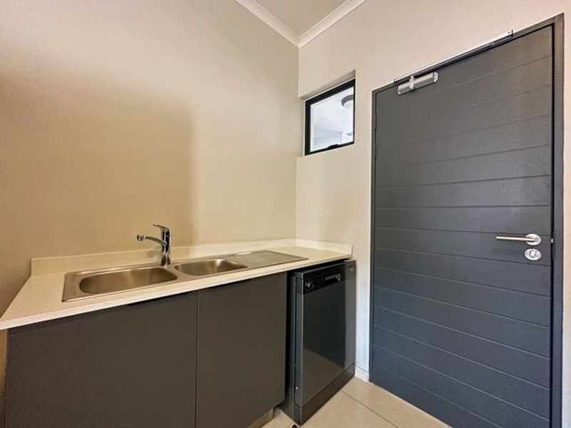 A clean and modern scullery area featuring a stainless steel double sink, integrated dishwasher, and sleek dark cabinetry with a matching door.
