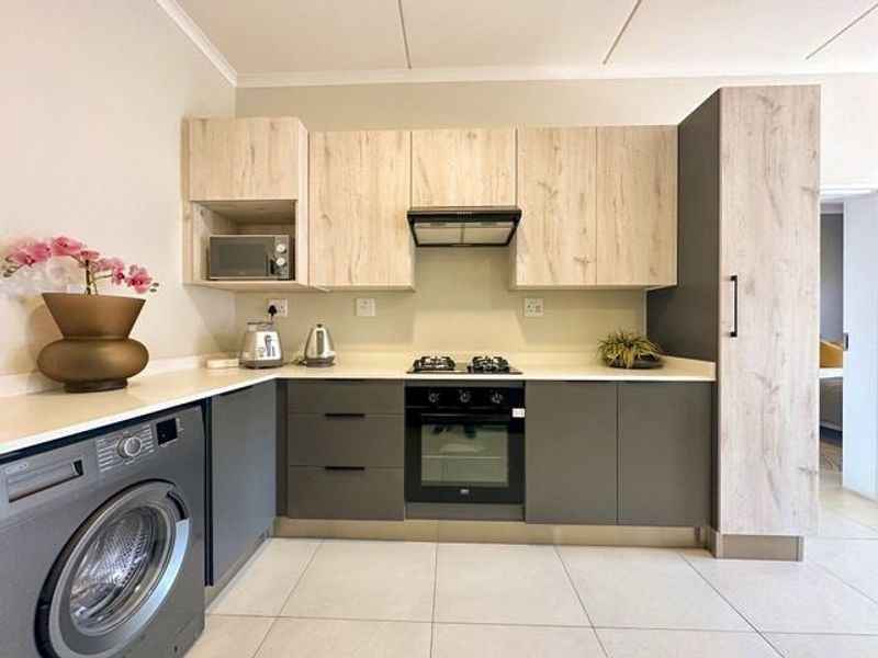 Modern kitchen featuring light wood and charcoal cabinetry, stone countertops, integrated gas hob, electric oven, extractor fan, and built-in microwave.