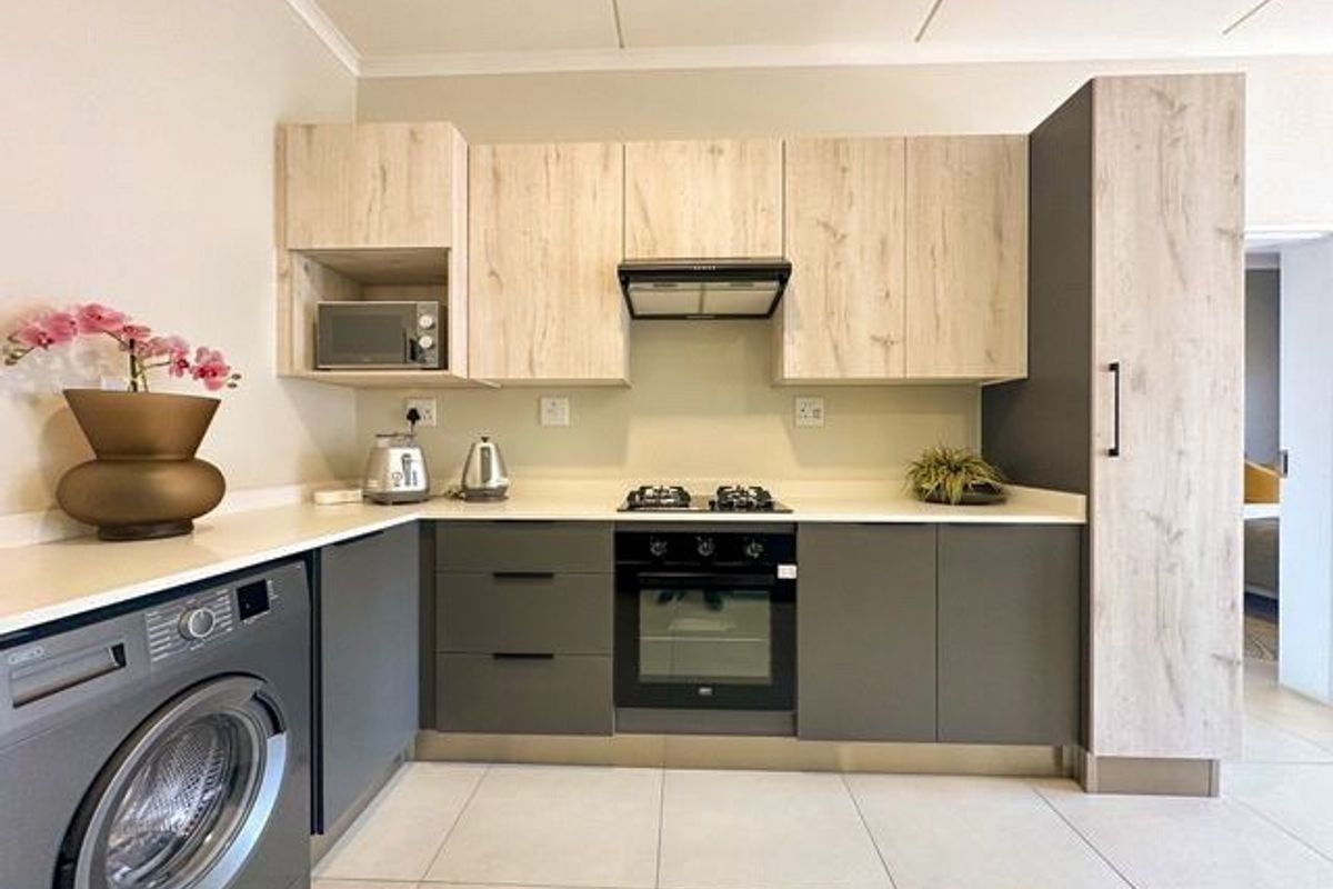 Modern kitchen featuring light wood and charcoal cabinetry, stone countertops, integrated gas hob, electric oven, extractor fan, and built-in microwave.