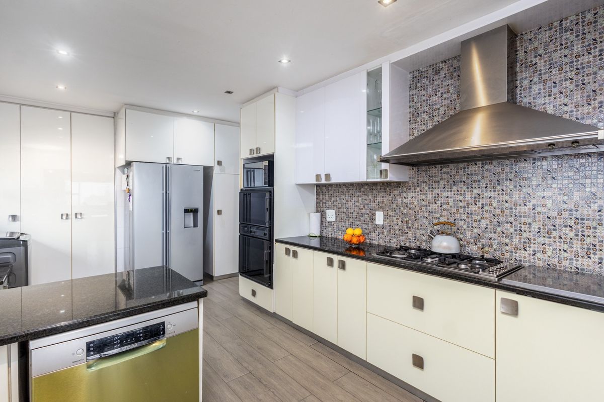 Modern kitchen featuring sleek cabinetry, granite countertops, a built-in oven, gas hob, stainless steel extractor fan, and decorative mosaic tile backsplash.